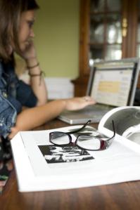 Female teen working at computer with a book and glasses in the foreground